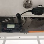 Marine VHF radio with coiled microphone cord tucked in a boat hatch, wiring visible around it.