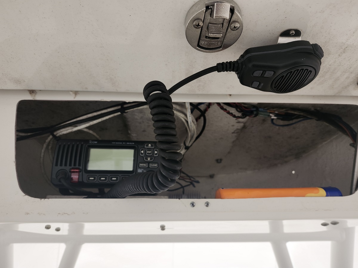 Marine VHF radio with coiled microphone cord tucked in a boat hatch, wiring visible around it.