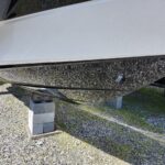White boat hull supported on concrete blocks on a gravel lot, viewed from underneath.