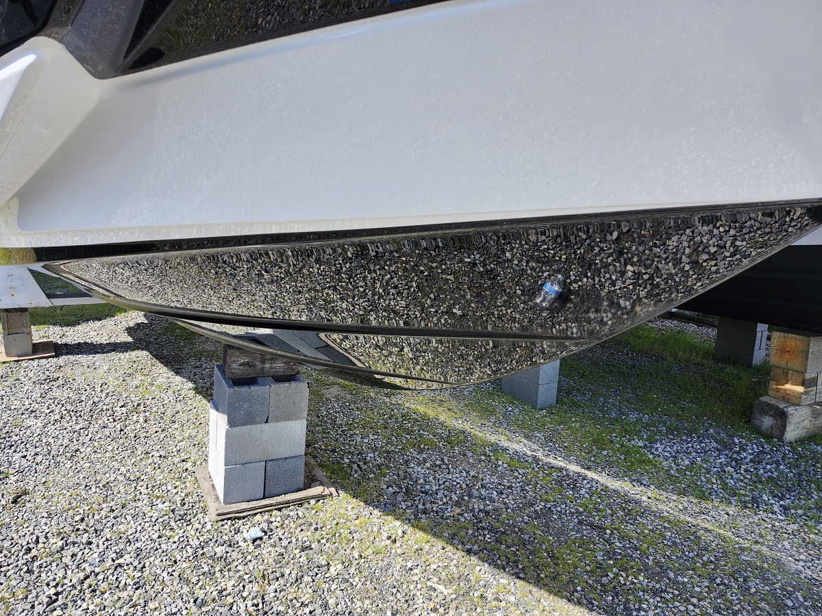 White boat hull supported on concrete blocks on a gravel lot, viewed from underneath.