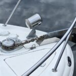 Close-up of a white boat bow showing a chrome windlass, anchor chain, and stainless rails with calm water in the background.