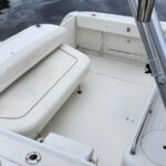 White boat deck with cushioned seating, storage hatch, and a folded bench on a calm body of water