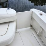White boat deck with cushioned seating, divider panel, and chrome rail by calm water.