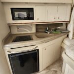 Compact boat galley: microwave on an upper shelf, sink and two-burner stove on a beige counter, with a small fridge below.