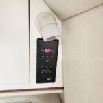 Wall-mounted black climate control panel with pink digital display showing 68, labeled cooling and heating, mounted beside a light beige wall and cabinet door.