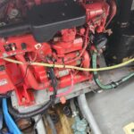Red marine diesel engine with black air intake, multiple hoses, and wiring visible in an engine compartment.