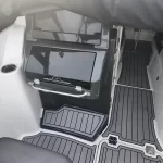 Boat cockpit interior with a gray built-in storage cabinet, stainless grab rail, and textured non-slip floor mats around a doorway to the cabin surface.