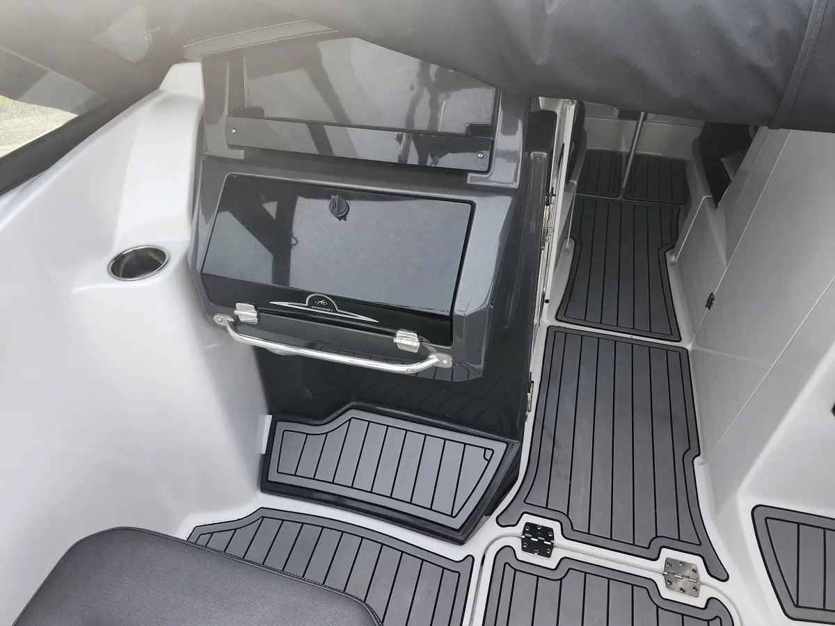 Boat cockpit interior with a gray built-in storage cabinet, stainless grab rail, and textured non-slip floor mats around a doorway to the cabin surface.