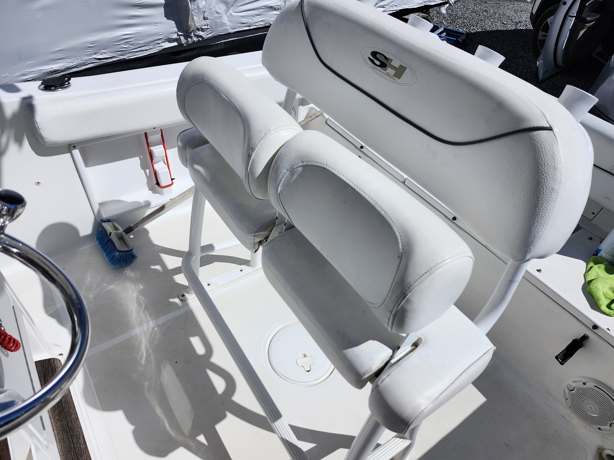 White cushioned boat seats and console on a deck, with a blue brush and red lanyard nearby.