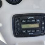 Marine stereo head unit on a white boat console, Infinity brand with Bluetooth label and numbered control buttons (volume, tune) and an LCD display.
