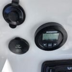 Humminbird marine display mounted on a boat console with a blank screen, adjacent to a USB/AUX input cover and a circular access cap nearby.