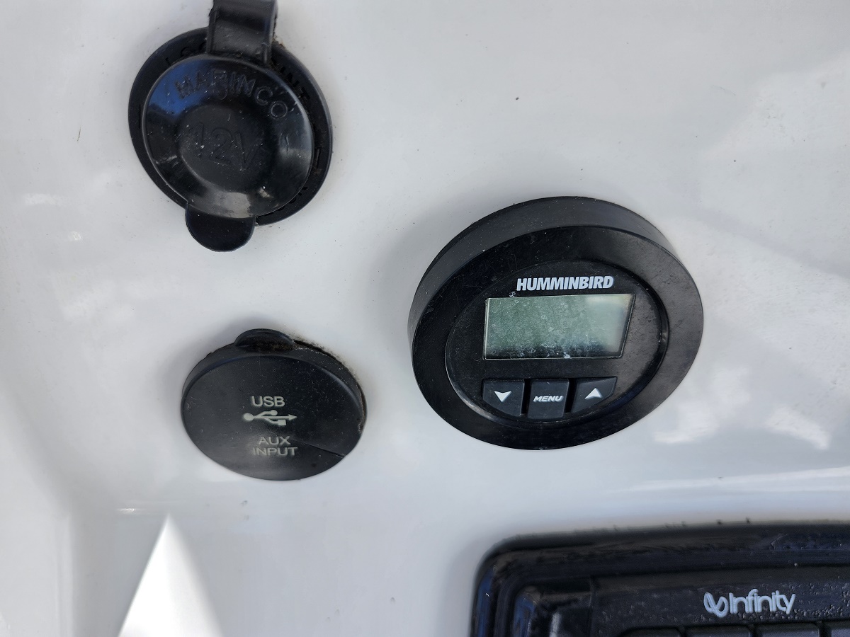 Humminbird marine display mounted on a boat console with a blank screen, adjacent to a USB/AUX input cover and a circular access cap nearby.