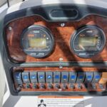 Boat helm panel with two round gauges (Speed and Tach) on a wood-grain dashboard and a row of blue toggle switches below I/O button labels visible on a sunny day