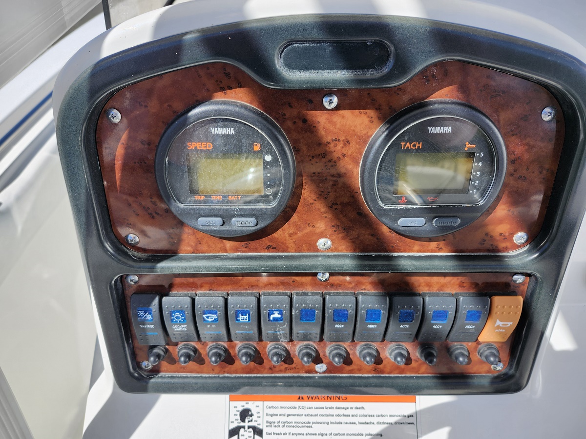 Boat helm panel with two round gauges (Speed and Tach) on a wood-grain dashboard and a row of blue toggle switches below I/O button labels visible on a sunny day