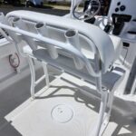 White boat deck with a fold-down seat and four vertical rod holders on the backrest; helm controls visible in background.