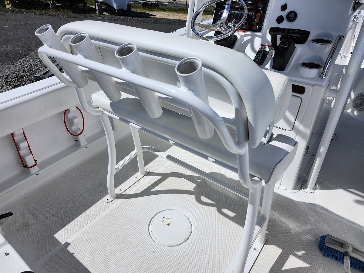 White boat deck with a fold-down seat and four vertical rod holders on the backrest; helm controls visible in background.