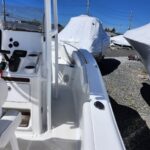 White motorboat cockpit with steering wheel, gauges, and seating, surrounded by other covered boats in a boatyard under a blue sky.