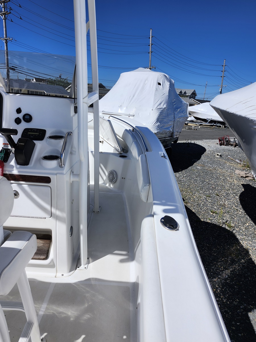 White motorboat cockpit with steering wheel, gauges, and seating, surrounded by other covered boats in a boatyard under a blue sky.
