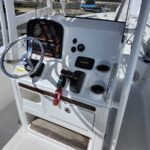 Close-up of a white boat cockpit showing a chrome steering wheel, instrument gauges, and control panel with key fobs hanging from the ignition near a wood-trimmed dashboard.