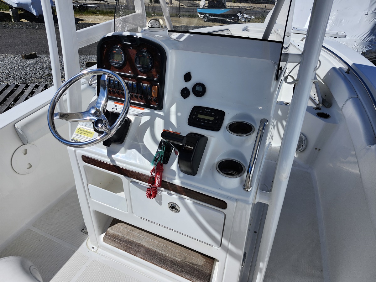 Close-up of a white boat cockpit showing a chrome steering wheel, instrument gauges, and control panel with key fobs hanging from the ignition near a wood-trimmed dashboard.