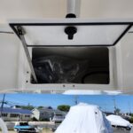 Open hatch on a white boat showing a cluttered storage compartment with a plastic bag inside, outdoors at a marina.