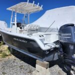 Black Sea Hunt boat on concrete blocks in a gravel lot, with a white-console cockpit and a Yamaha 150 outboard motor attached to the stern under a clear blue sky.