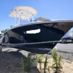 Large dark boat on blocks in a boatyard, blue hull, view of bow with t-top/tower overhead and other boats nearby.