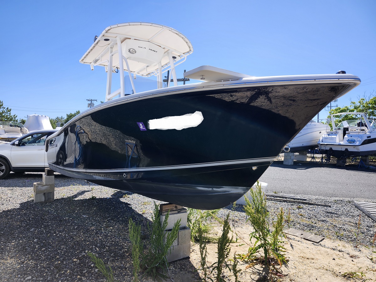 Large dark boat on blocks in a boatyard, blue hull, view of bow with t-top/tower overhead and other boats nearby.