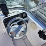 Boat captain's helm with a light-gray steering wheel, gauges, and a mounted electronics device inside a white cockpit on a sunny day inshore.