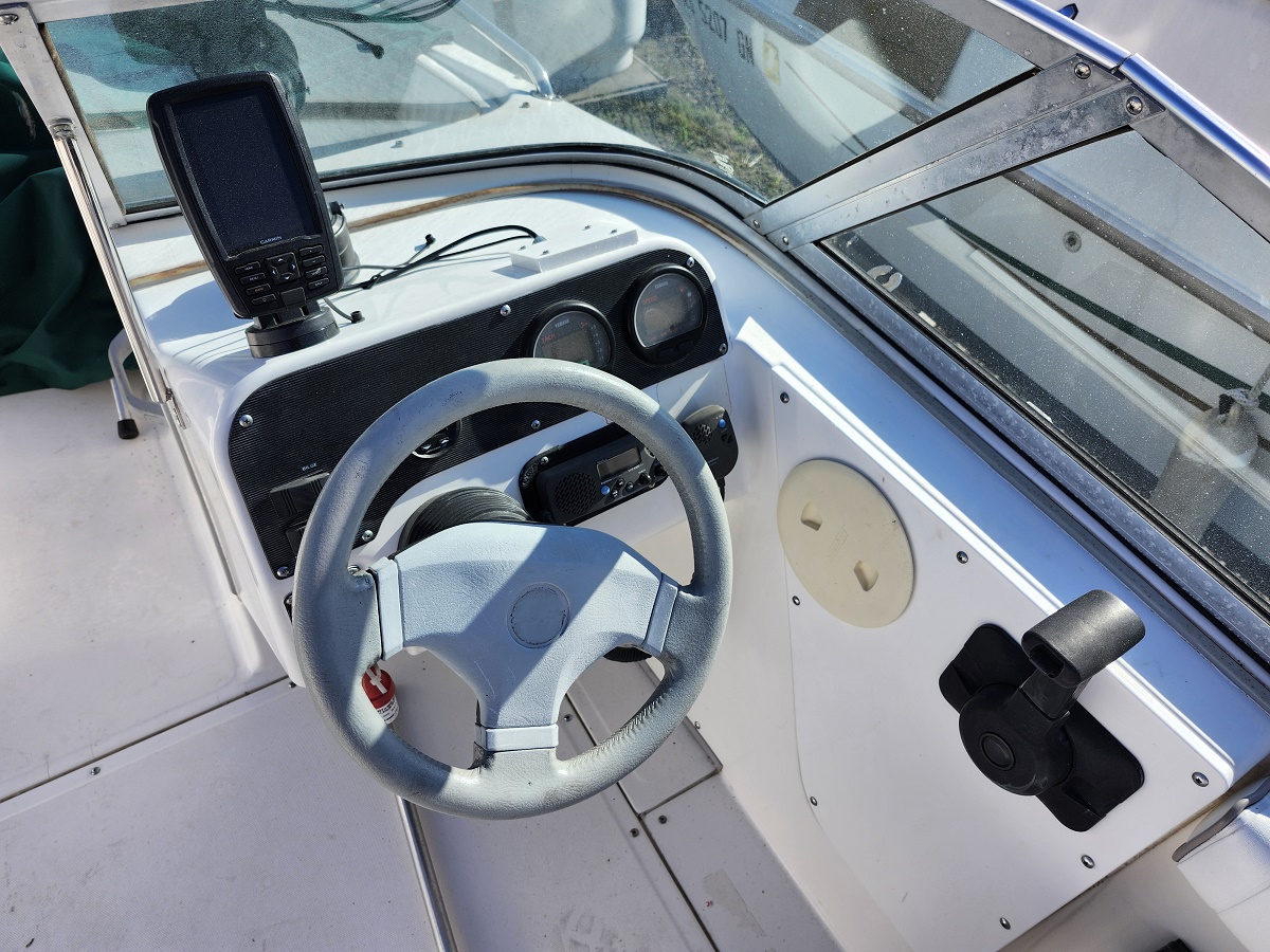 Boat captain's helm with a light-gray steering wheel, gauges, and a mounted electronics device inside a white cockpit on a sunny day inshore.