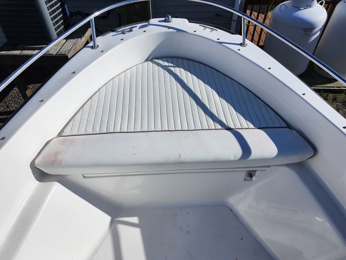 Open bow of a white motorboat showing a curved cushioned deck pad, ribbed foredeck, and stainless railing.