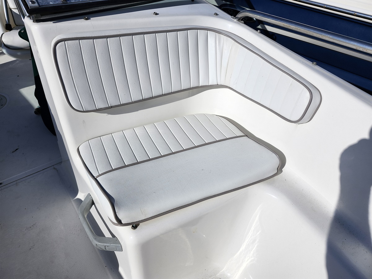 White boat seating with padded back and seat cushions, light gray piping, on a sunny deck.