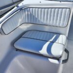 White vinyl boat bench seating with light blue piping, built-in backrest and cushion on a sunlit deck.