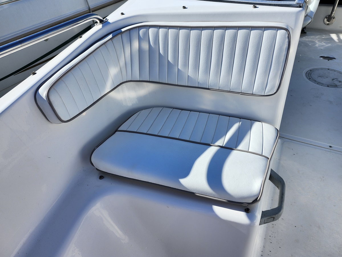 White vinyl boat bench seating with light blue piping, built-in backrest and cushion on a sunlit deck.