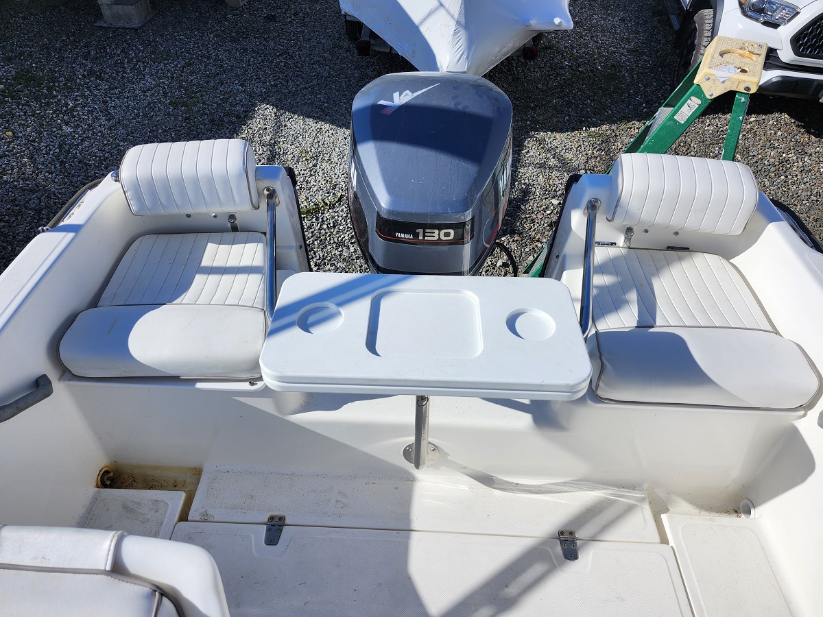 White boat cockpit with two cushioned bench seats, a small fold-down table with two cup holders, and a Yamaha 130 outboard motor at the rear.