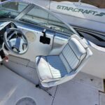 Boat cockpit with light blue steering wheel and white captain seat; control panel and throttle visible, Starcraft boat in background.