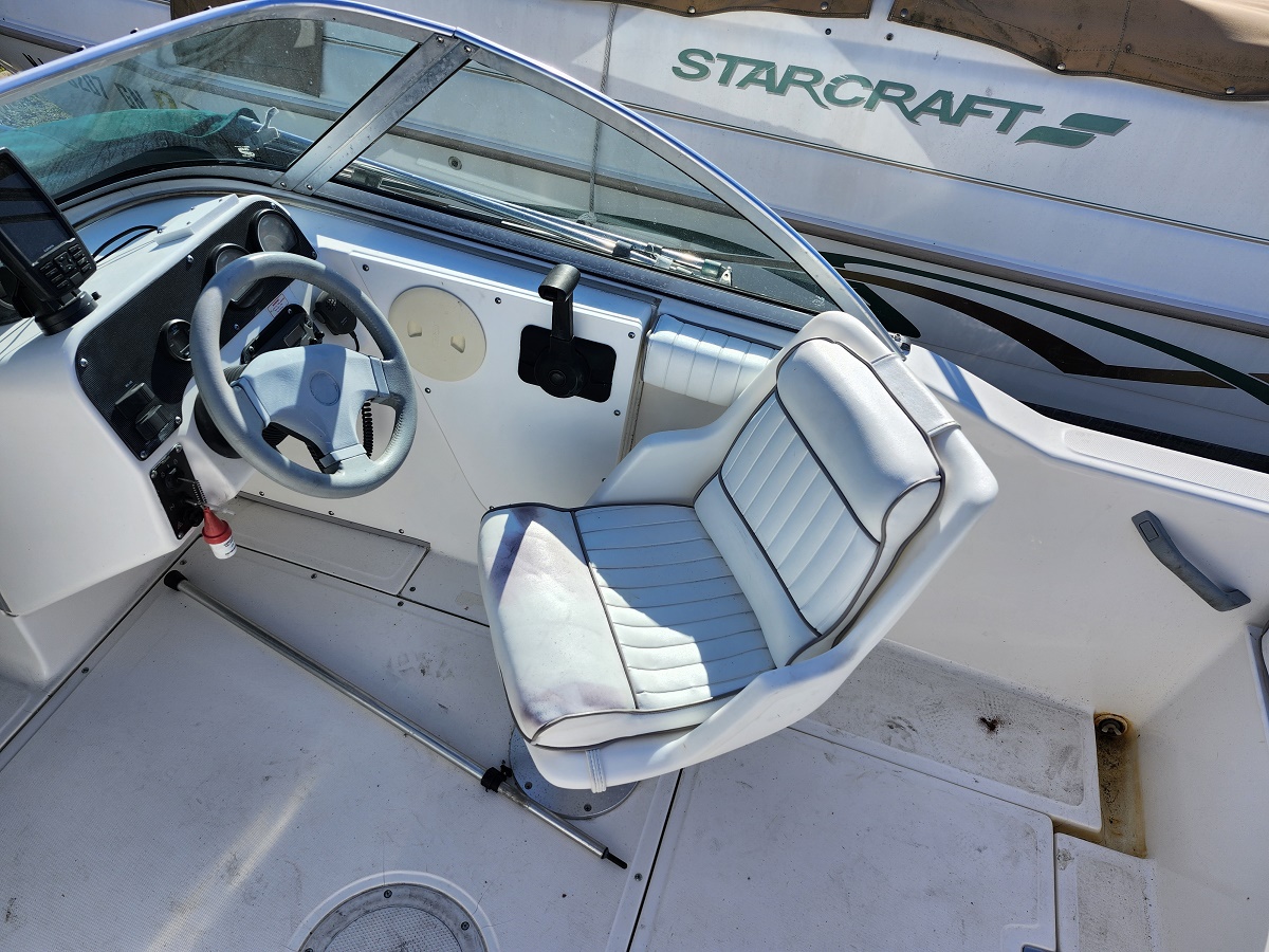 Boat cockpit with light blue steering wheel and white captain seat; control panel and throttle visible, Starcraft boat in background.