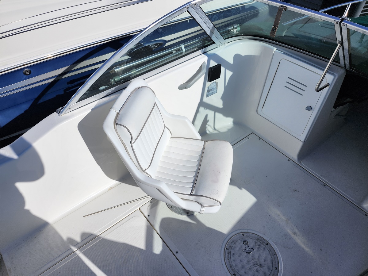 White captain's chair on a motorboat deck with curved windshield and nearby storage locker door