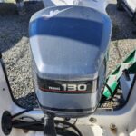Close-up of a gray Yamaha 130 outboard motor mounted on the stern of a white boat, with a dusty cowling and visible cables.