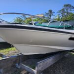 White motorboat on a trailer in a boat lot, bow facing the camera with a chrome railing and blue sky above.