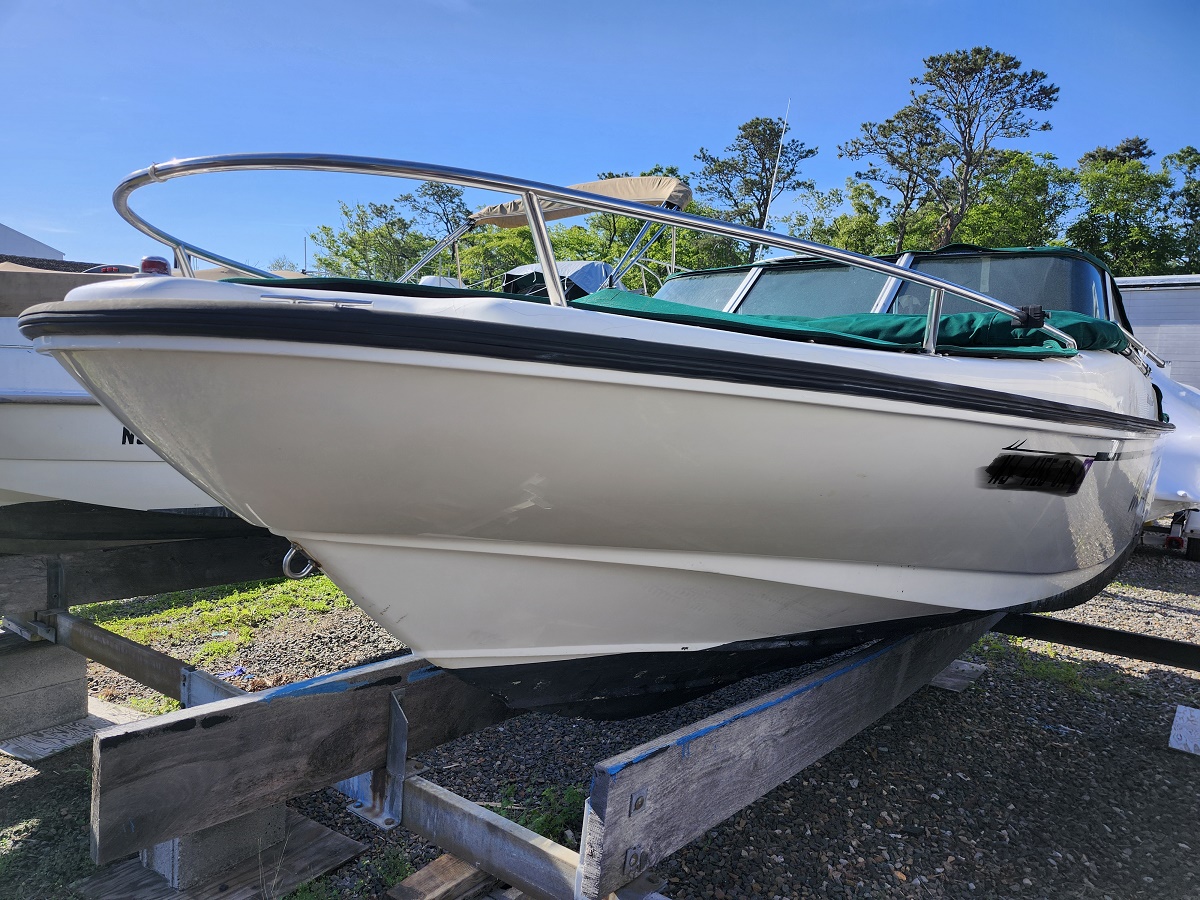 White motorboat on a trailer in a boat lot, bow facing the camera with a chrome railing and blue sky above.