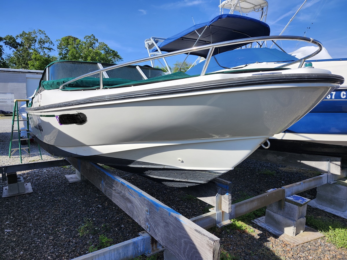 White motorboat on a cradle in a boatyard, covered with a blue canopy and surrounded by gravel and other boats.