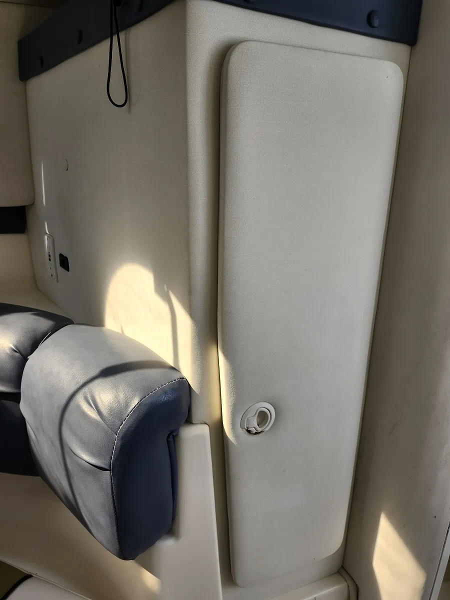 Beige vehicle interior with a padded vertical panel, blue armrest, and a circular cup holder opening on the panel.