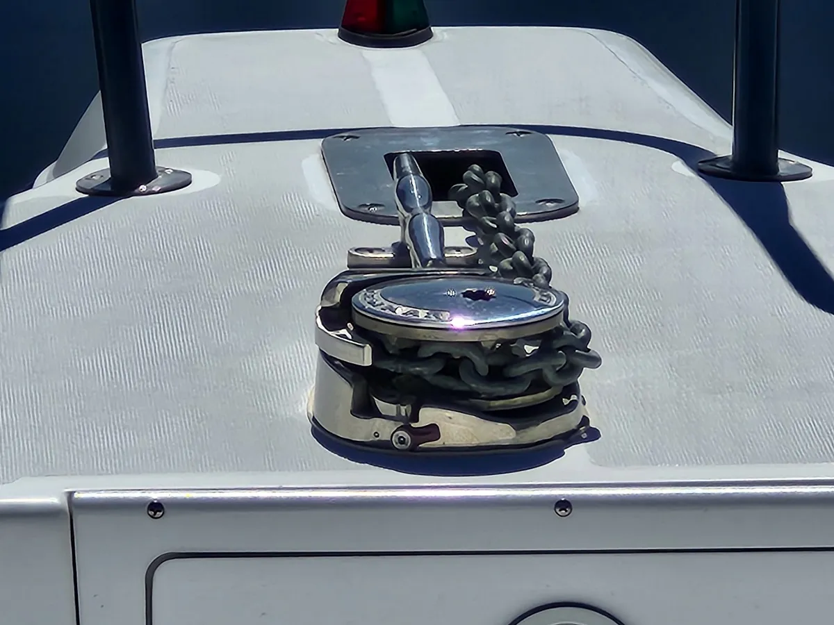 Anchor windlass with chain on the bow of a boat, chrome cleat and anchor chain ready for retrieval.