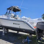 Century motorboat on block stands in a gravel boatyard with a covered Suzuki outboard engine