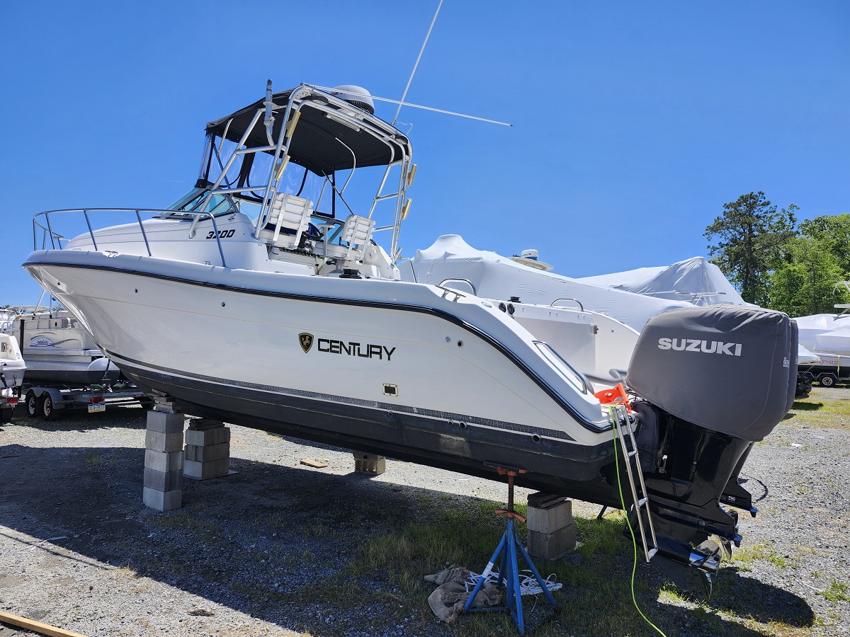 Century motorboat on block stands in a gravel boatyard with a covered Suzuki outboard engine