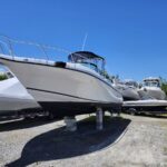 White motorboat on concrete blocks in a boatyard with other boats covered or on trailers under a bright blue sky
