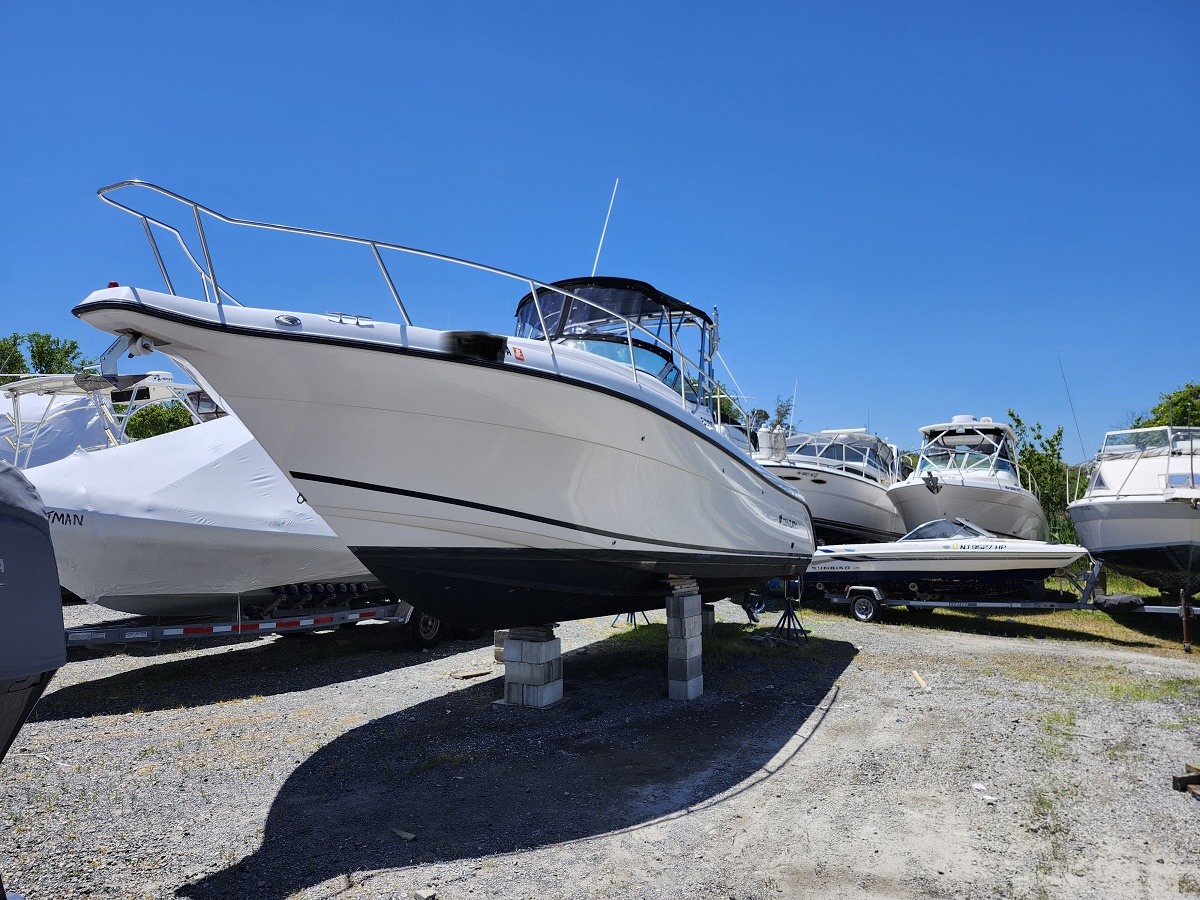 White motorboat on concrete blocks in a boatyard with other boats covered or on trailers under a bright blue sky