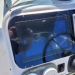 Boat helm featuring a reflective glass touchscreen display mounted at the console, with a Raymarine screen nearby in the cockpit, and a steering wheel visible in the background.