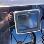 Raymarine marine display mounted on a boat helm with routed cables; photographer's reflection visible in the screen glass.